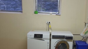 A laundry room with a front-loading washer and dryer, a window with a view, and a blue laundry basket. - Lischa 3. OG Süd Appartement/Fewo, Dusche oder Bad, WC by Interhome (Fiesch)