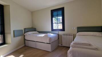 Un dormitorio con dos camas, una ventana, un radiador y una lámpara fijada a la pared.