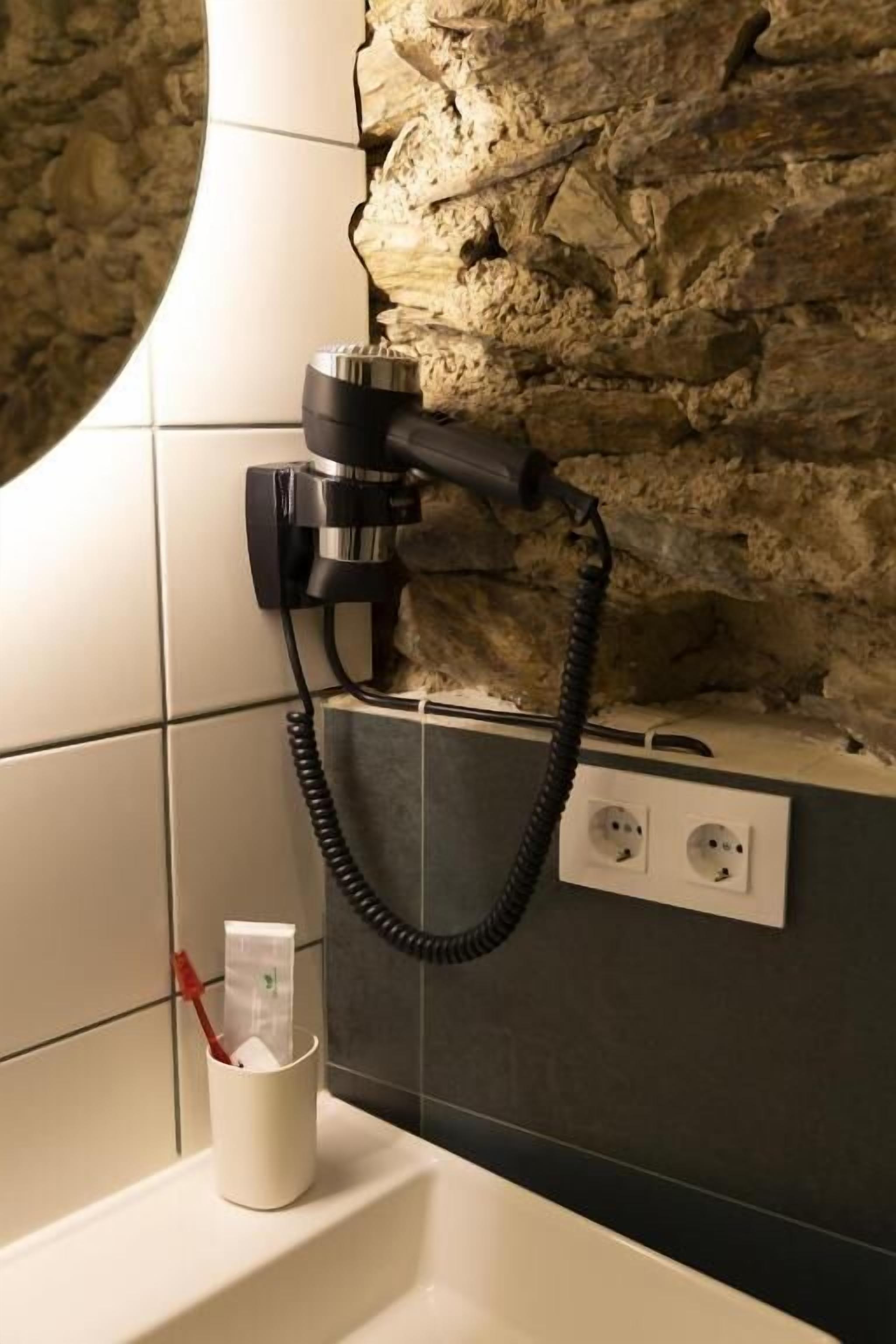 Un bany amb paret de pedra, un assecador de cabells fixat a la paret i una tassa amb un estotxa dits.