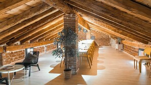 Um espaço no sótão com vigas de madeira expostas, paredes de tijolo e um pilar central com uma planta em vaso.