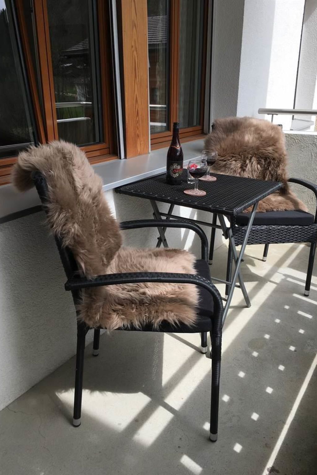 Une terrasse avec deux chaises et une table, une bouteille et deux verres de vin rouge.