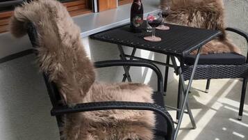 Une terrasse avec deux chaises et une table, une bouteille et deux verres de vin rouge.