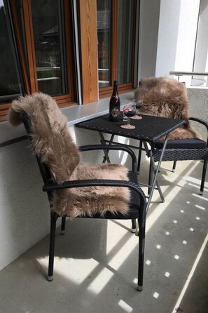 A patio with two chairs and a table, a bottle, and two glasses of red wine.