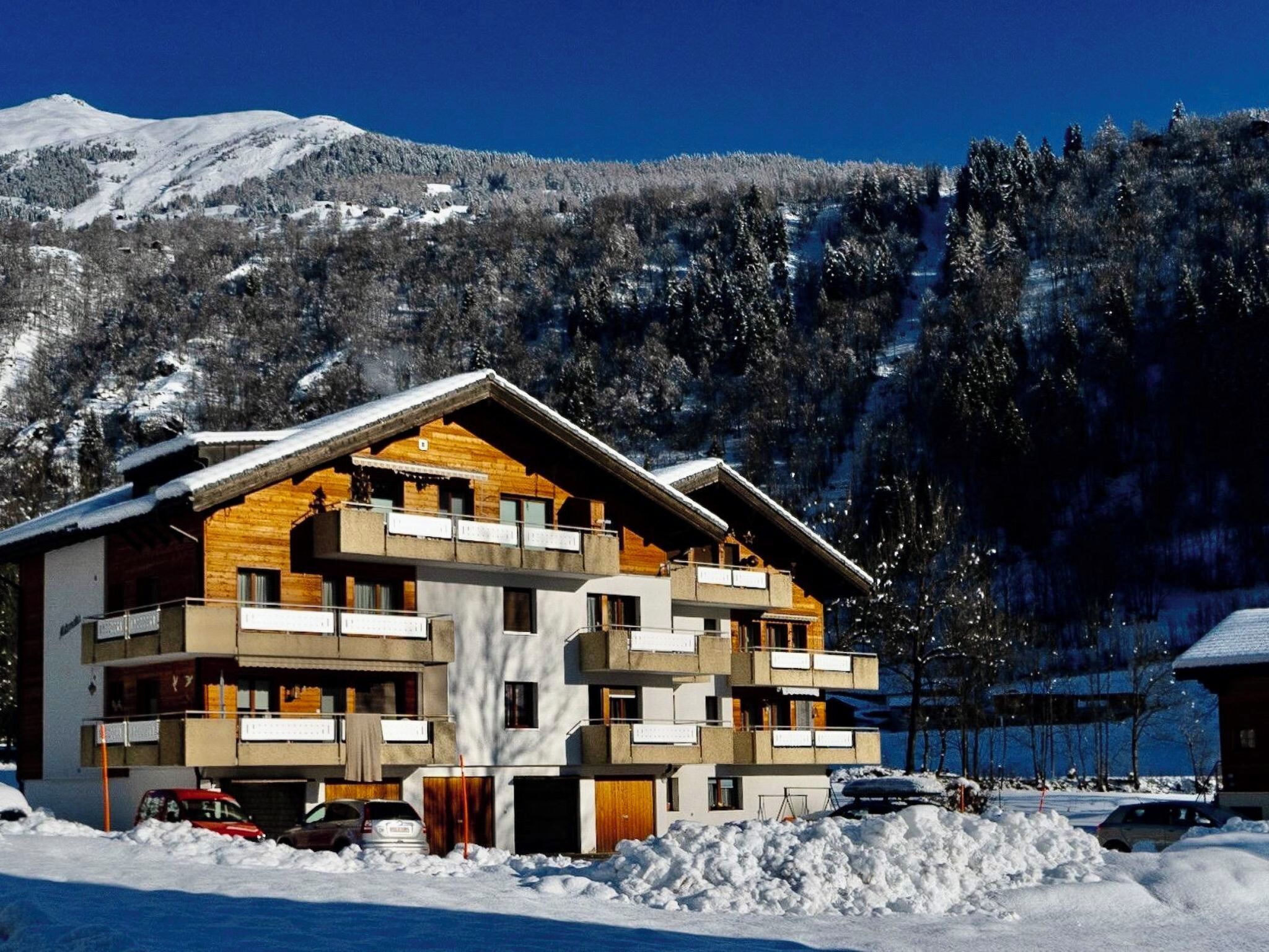 Un hôtel à plusieurs étages doté de balcons, avec une piste de ski en arrière-plan et un paysage montagneux.