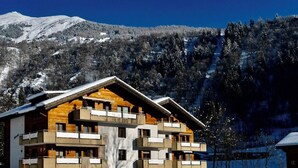 A multi-story hotel with balconies, a ski slope in the background, and a mountainous landscape. - Milimatta 1 1. OG Süd Studio, Dusche oder Bad, WC 1 1/2 Zimmerwohnung, 2-Betten by Interhome (Fiesch)