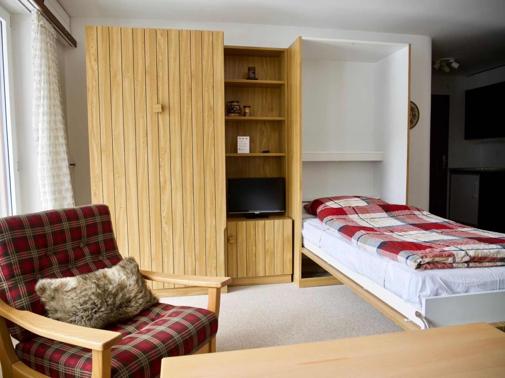 Une petite pièce comprenant un lit, une chaise, un téléviseur et une armoire en bois.