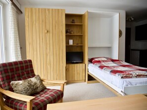 Une petite pièce comprenant un lit, une chaise, un téléviseur et une armoire en bois.