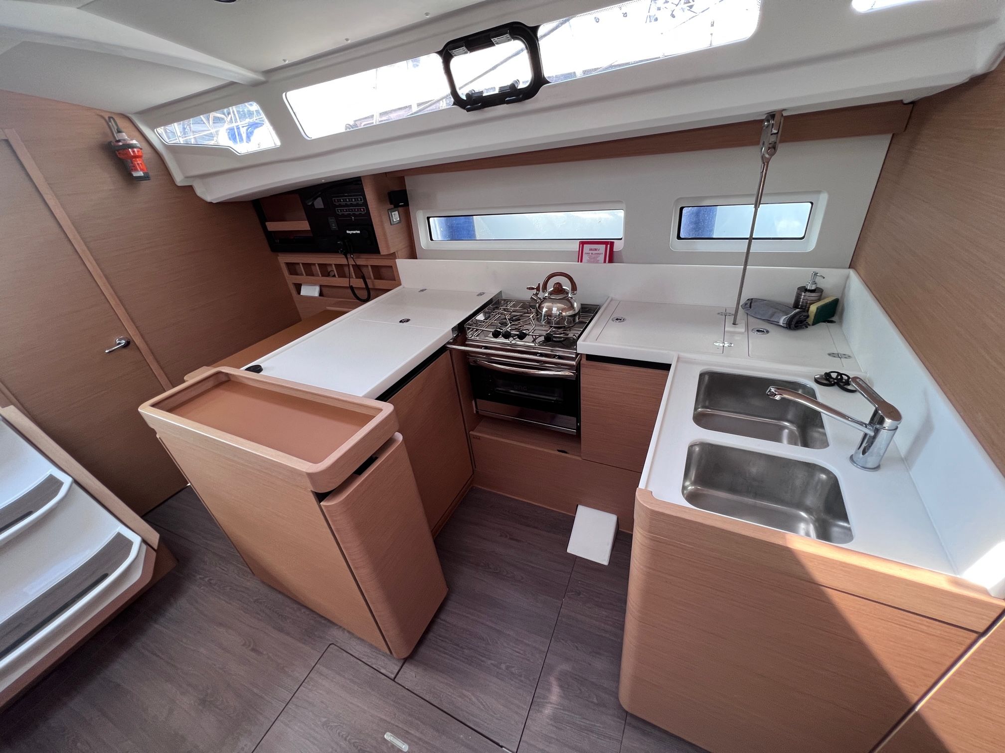 A compact galley with a stove, sink, and storage cabinets, featuring skylights and a view of the sky.