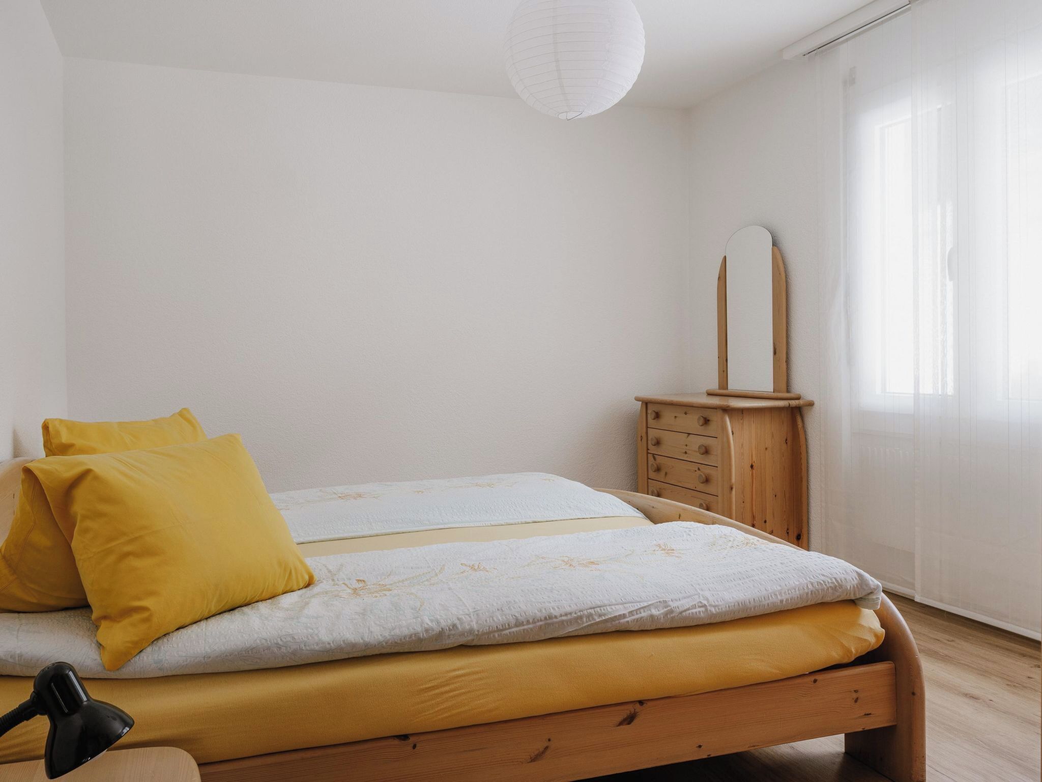 Une chambre à coucher avec un lit en bois, une table de chevet avec un miroir et une lampe.