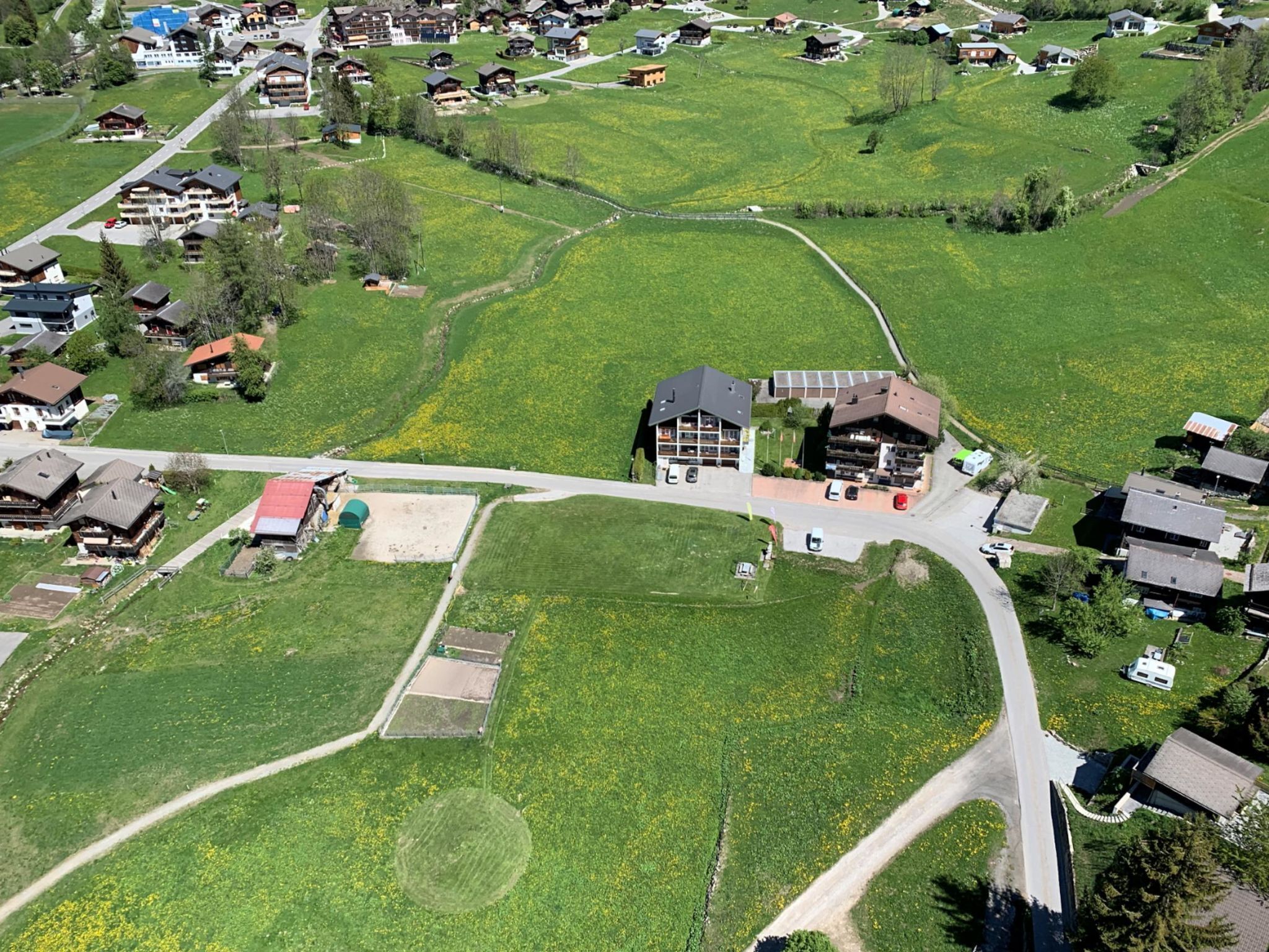 Une vue aérienne d’une zone rurale, avec un grand bâtiment entouré de champs verdoyants et de maisons plus petites.