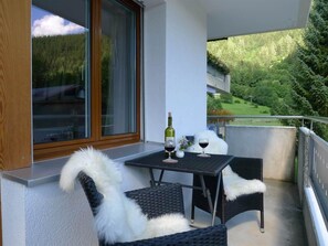 Ein Balkon mit Tisch, zwei Stühlen, einer Weinflasche und einem Weinglas.
