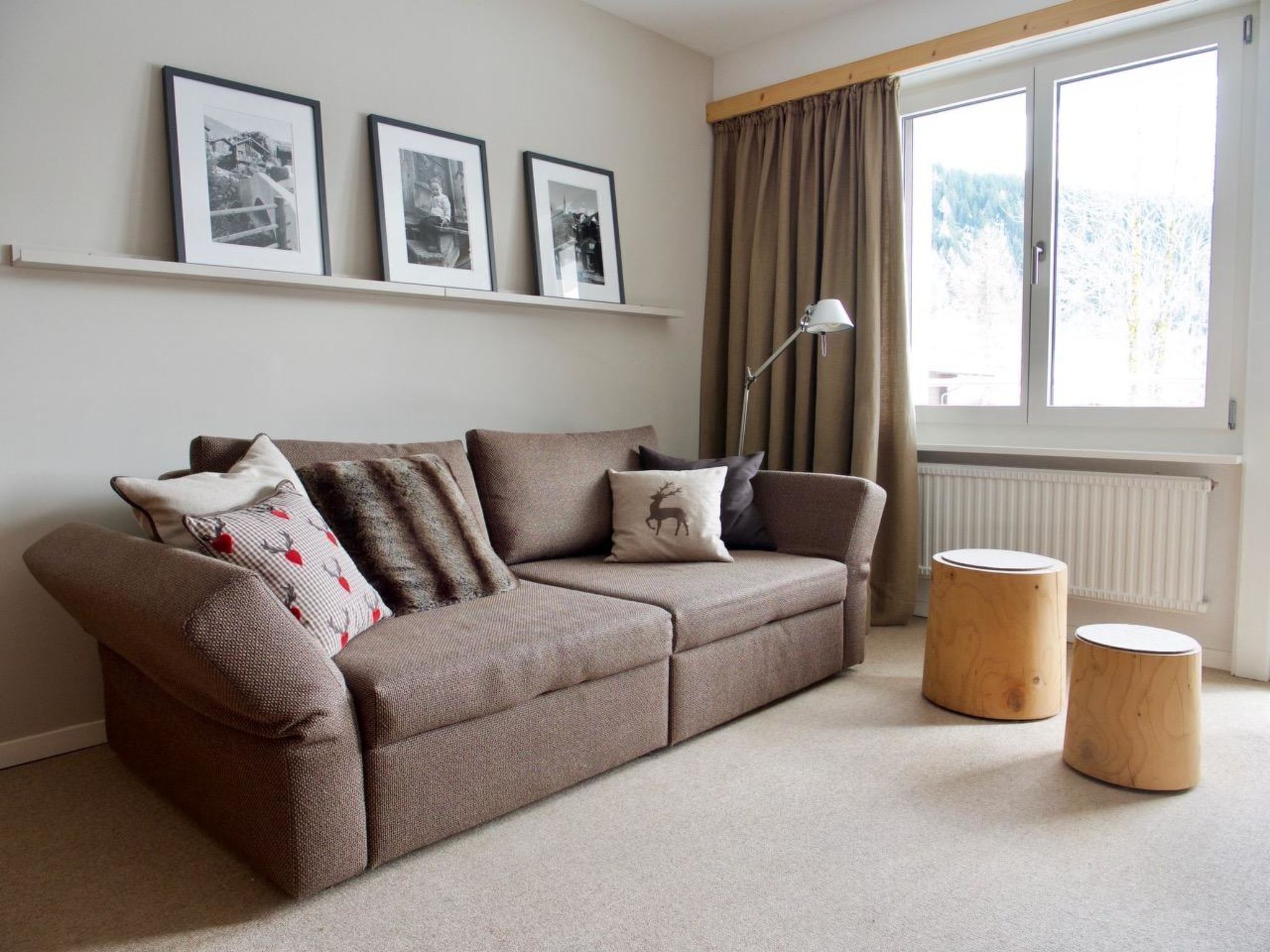 A living room with a sofa, two side tables, a radiator, and three framed pictures on the wall.