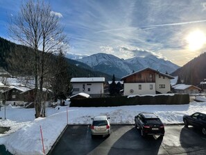 Ein Parkplatz mit schneebedecktem Boden, ein Gebäude mit Holzfassade und schneebedeckte Berge im Hintergrund.