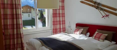 Een slaapkamer met een bed, gordijnen, een raam en een ski-rek aan de muur.