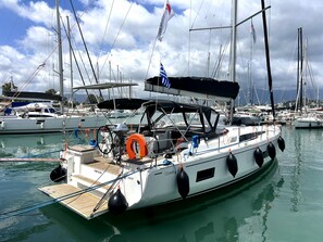 Eine Segelyacht liegt in einer Marina, wo mehrere Boote vor Anker liegen, mit einer überdachten Terrasse und einem Rettungsreifen.