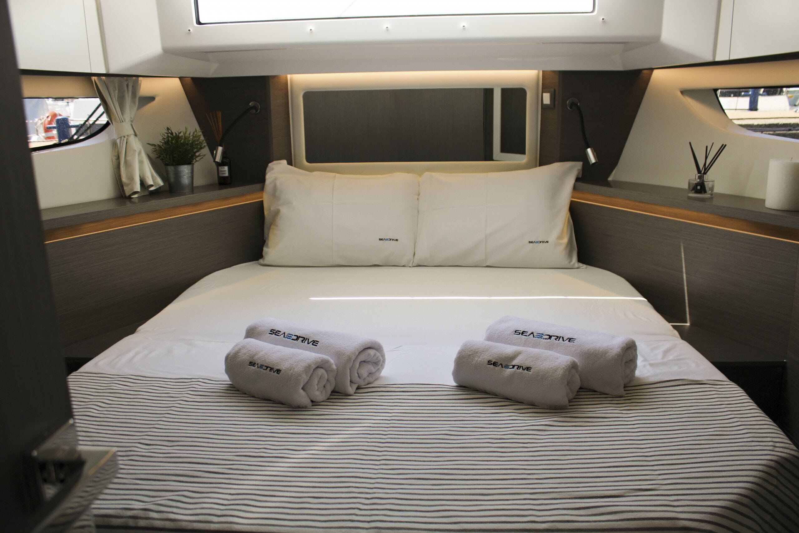 A bed with two rolled towels, a headboard, bedside tables, and a window.