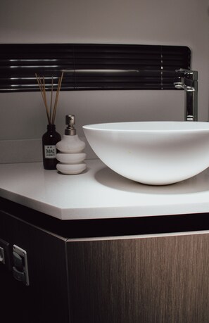 A bathroom vanity with a white sink, a dark bottle with a label, and a set of reed diffusers.