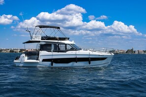 Un barco a motor blanco con cabina y plataforma superior, navegando en el agua.