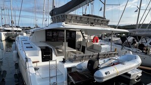 Un yate blanco amarrado en un puerto deportivo, con una zona de estar cubierta, un bote inflable pequeño y un flotador salvavidas.