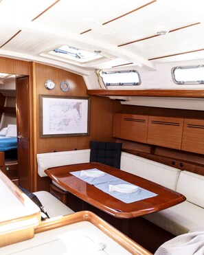 A boat interior with a dining area, wooden cabinetry, a map on the wall, and a window above the table. - Sun-Kissed Sailing Adventure in the Ionian Islands (Nidri)