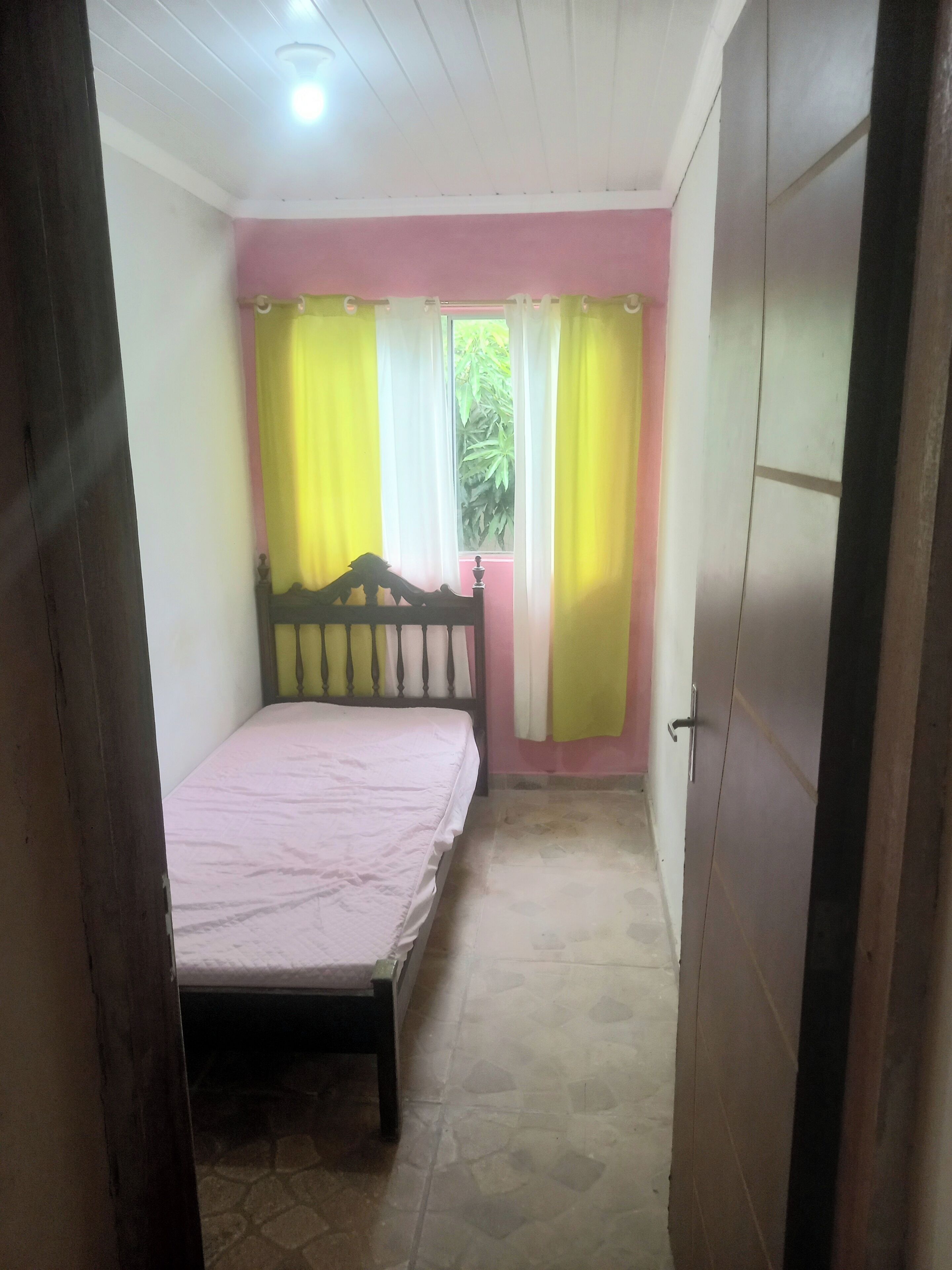 A bedroom with a bed, a window with curtains, a door, and a tiled floor.