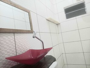 Een badkamer met een rode wasbak, een spiegel en een ventilatie rooster.