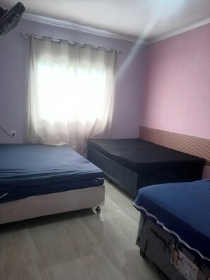 Een kamer met twee bedden, een raam met gordijnen, een roze wand en een plafondventilator.