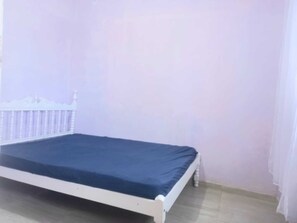 Een enkel bed met een wit frame en een donkerblauwe matras in een kamer met lichte muren en een witte vloer.