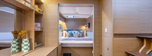 A compact room with a bed, a small table, and a shelf with books and decorative items. - Sun-Kissed Sailing Adventure in the Ionian Islands, Lefkada (Lefkada)