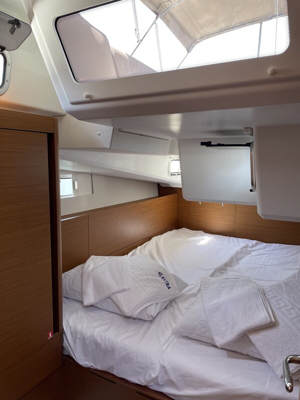 A compact, well-lit cabin with a bed, wooden headboard, and a skylight.