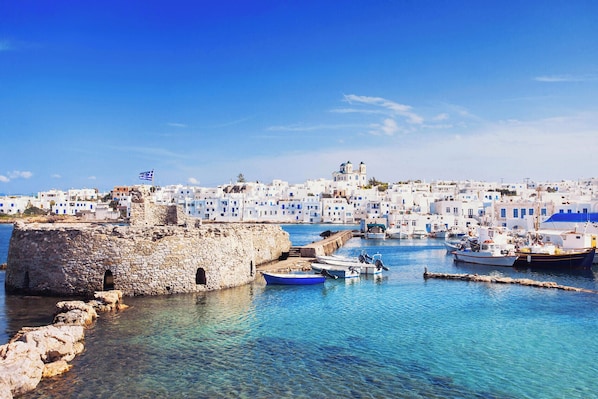 A coastal town with stone buildings, a clear blue sky, and boats in the harbor.