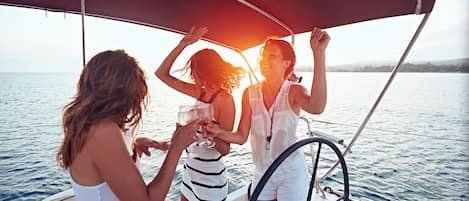 Eine Segelyacht mit Sonnensegel, Personen mit Getränken und ruhiges Meer.