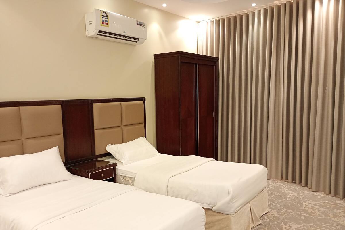 Quarto de hotel com duas camas, um guarda-roupa, um aparelho de ar condicionado e uma cortina.