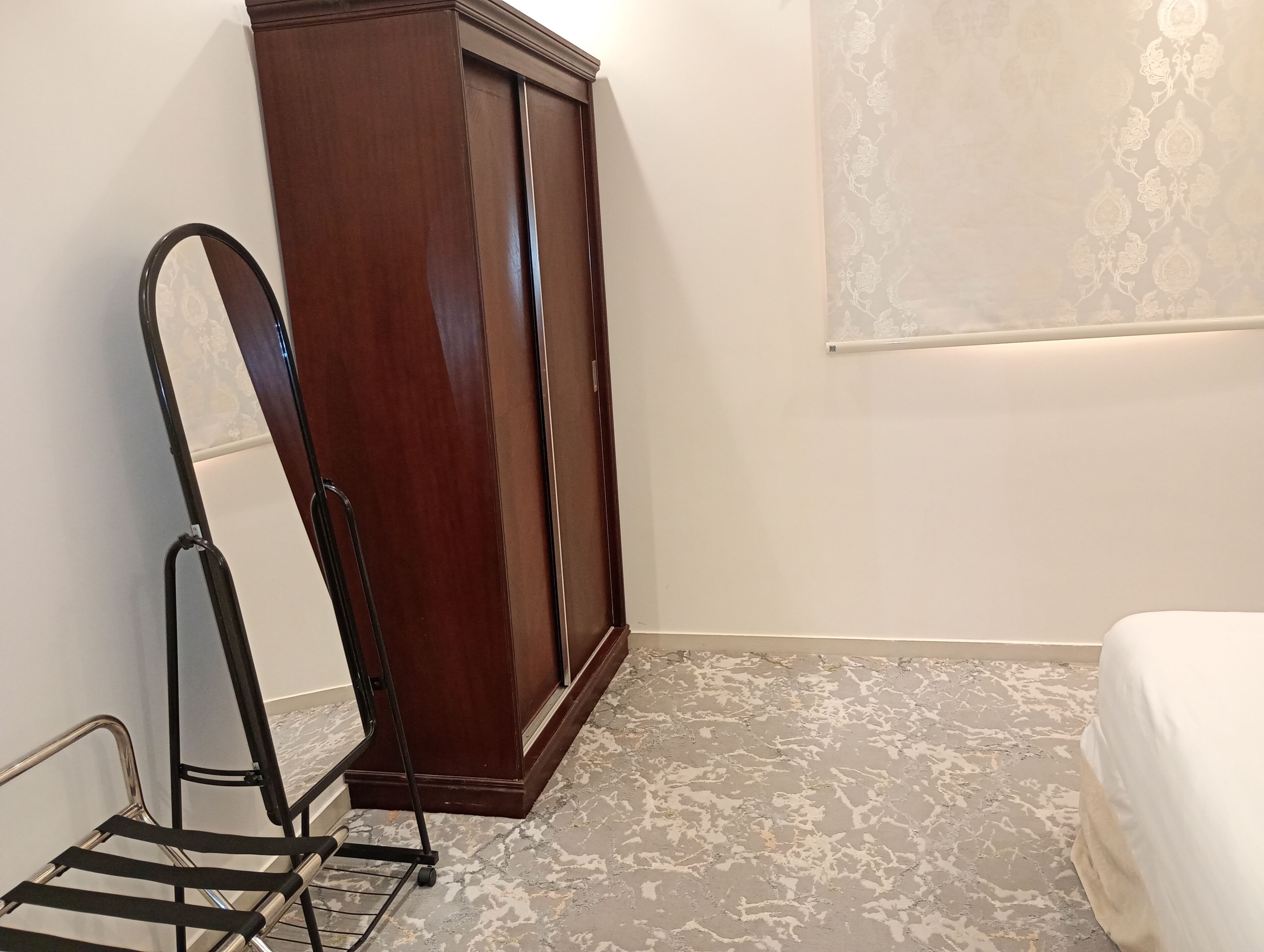 A bedroom with a wooden wardrobe, a mirror, a metal chair, and a bed.