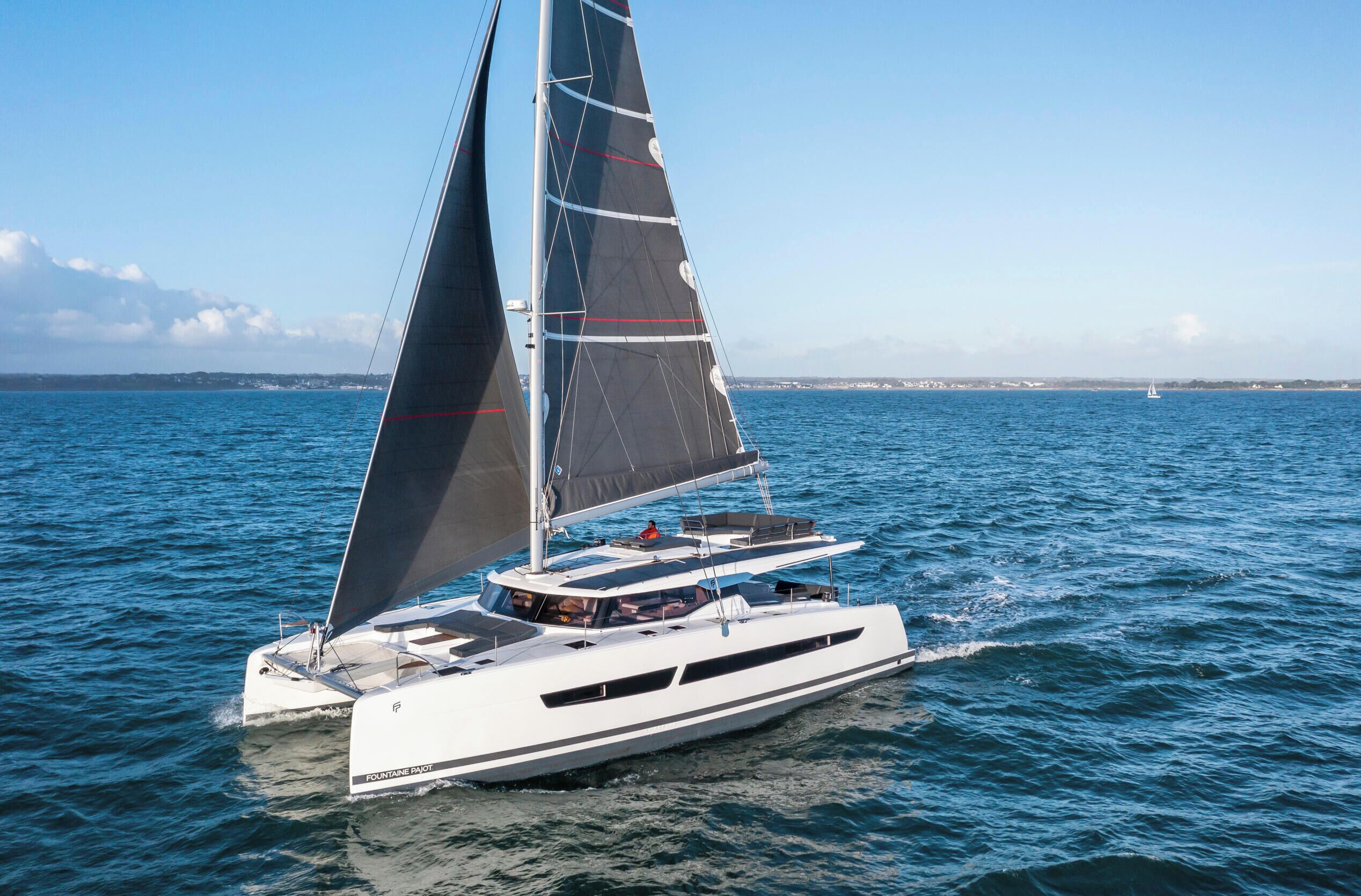 A white yacht with a sleek design, multiple decks, and a prominent sail.