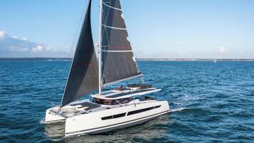 A white yacht with a sleek design, multiple decks, and a prominent sail.