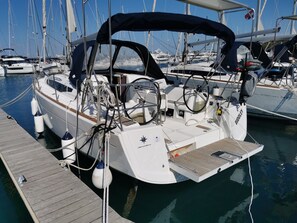 Un velero amarrado en una marina, con cabina cubierta, winch y timón a estribor.