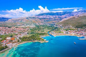 An aerial view of a coastal town with a marina, clear blue waters, and mountainous background.