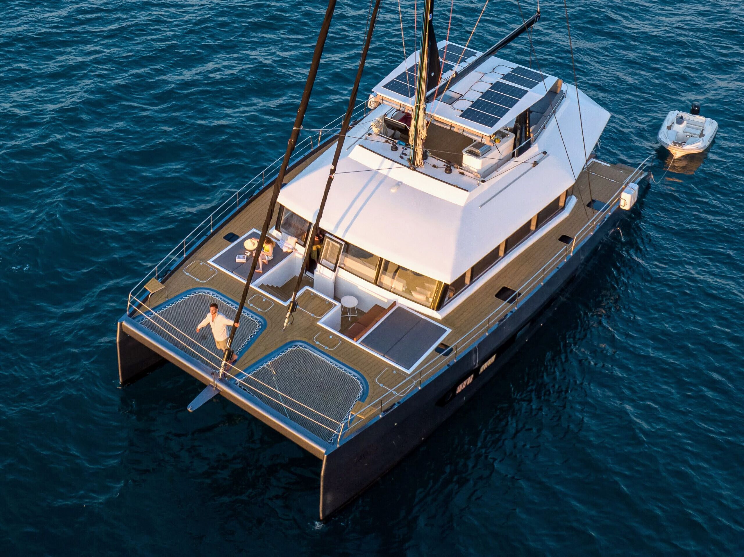 A sailboat with a deck area, a small boat docked nearby, and a person standing on the deck.