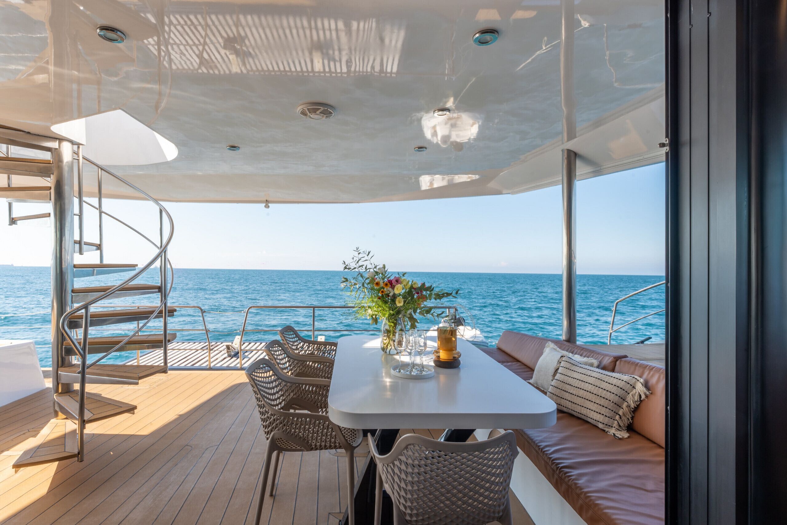 A yacht deck with a table, chairs, and a sofa, overlooking the sea.
