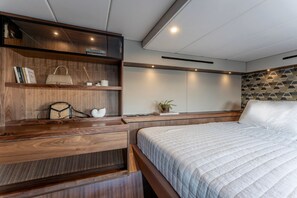 A bedroom with a large bed, wooden shelving with books and a handbag, a bedside table with a plant, and a geometric-patterned wall. - Sun-Kissed Sailing Adventure in the Saronic Islands (Lavrio)
