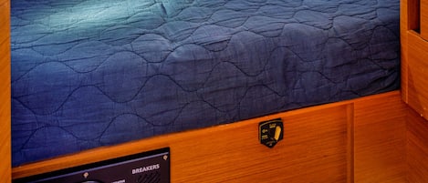 Une cabine compacte et bien éclairée, équipée d’un lit simple, d’un panneau de contrôle avec des disjoncteurs et d’une petite fenêtre.