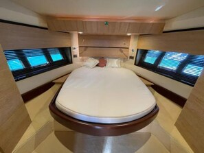 Una cama con cabecera, dos ventanas con persianas e iluminación empotrada en el techo.