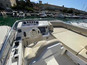 A boat's interior with a steering wheel, control panel, and seating area.