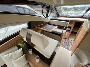 A boat interior with a cushioned seating area, a small table, and a view of the marina. - Sun-Kissed Sailing Adventure in Sibenik, Croatia (Primošten)