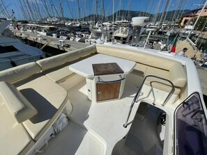 A boat with a cushioned seating area, a small table, and a mounted device.