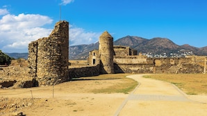 An ancient stone structure with a pathway leading through ruins, surrounded by mountains and a clear sky. - Sun-Kissed Sailing Adventure in Cataluña (Rosas / Roses)