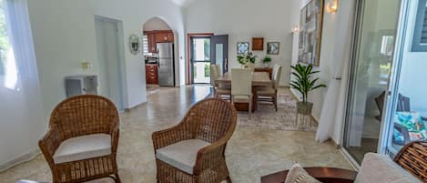 Amplia sala de estar con mobiliario de mimbre, una mesa de comedor y una cocina al fondo.