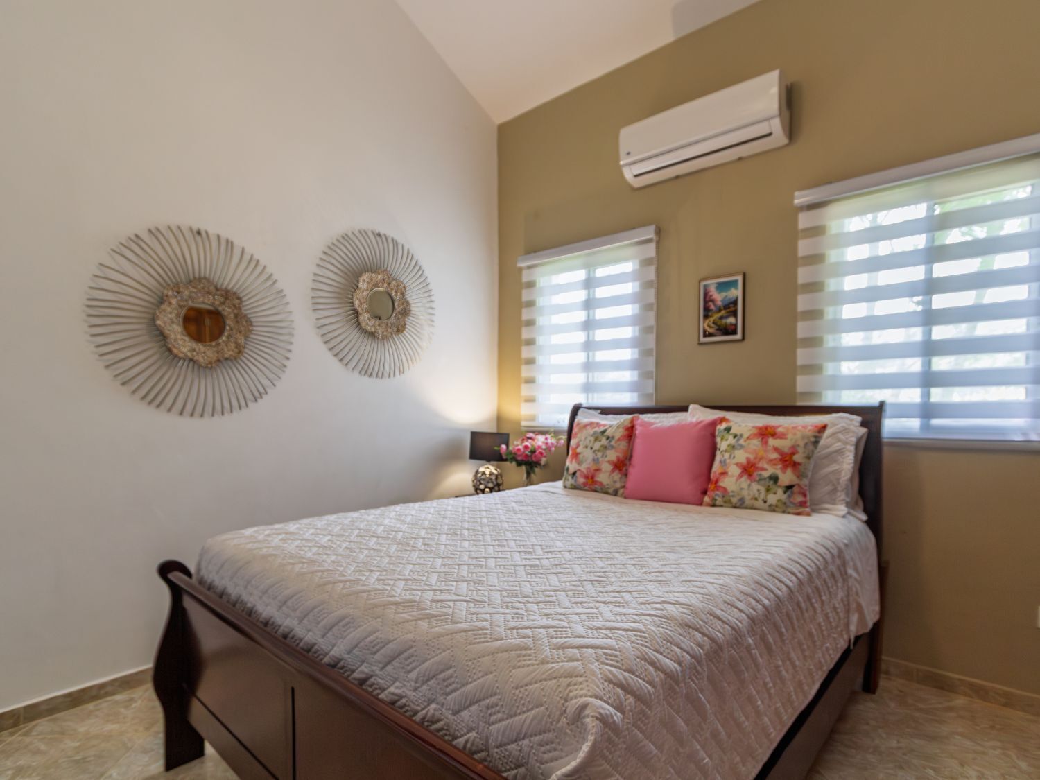 A bedroom with a bed, two wall decorations, an air conditioner, and a window with blinds.