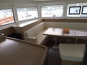 A boat interior with a cushioned seating area, a table, and windows with views of the water. - Sun-Kissed Sailing Adventure in the Ionian Islands, Lefkada (Lefkada)